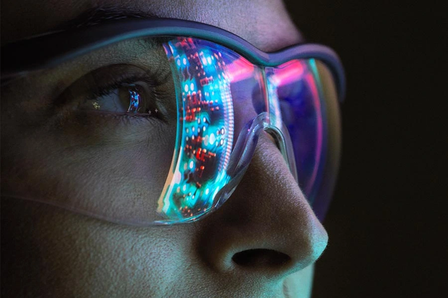 Lighted electronics reflecting off of a woman's safety glasses in a lab.