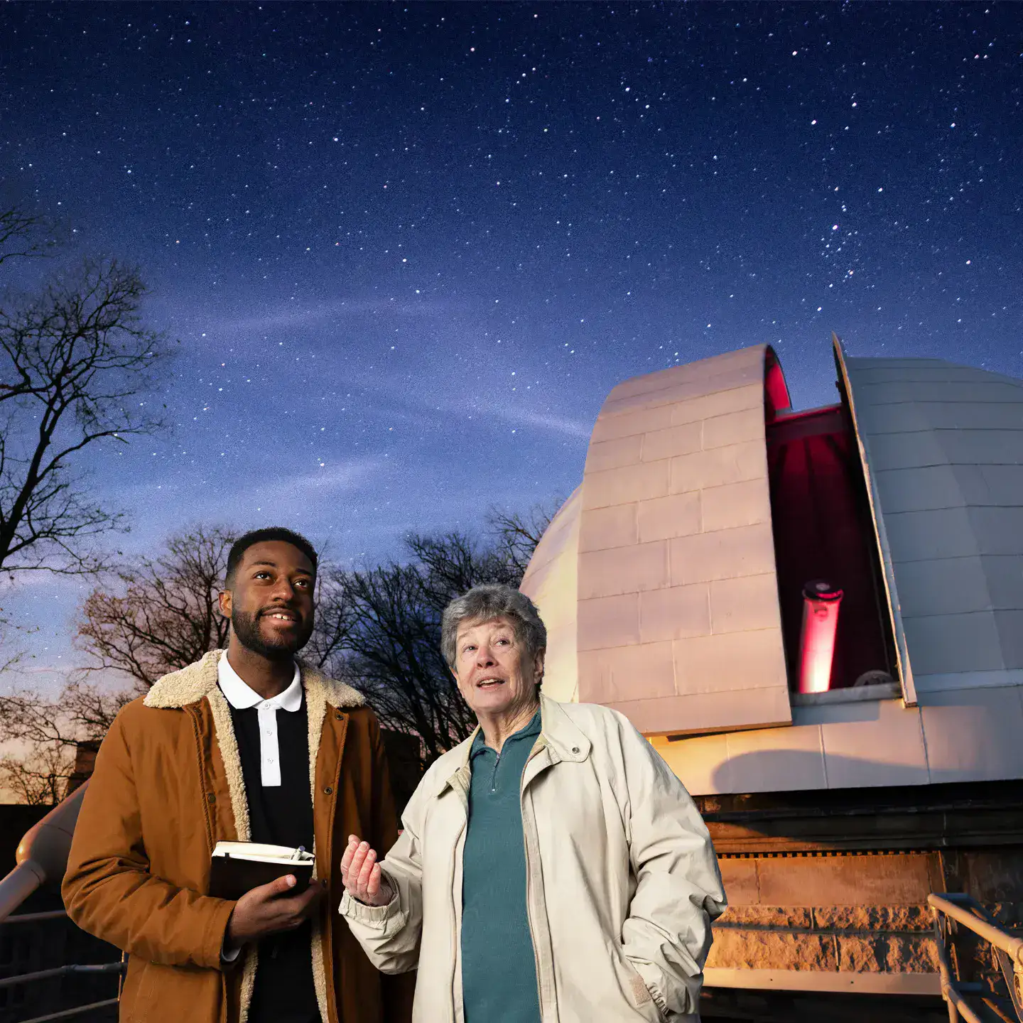 An astronomy professor and her student stand outside in front of an observatory discussing the night sky.
