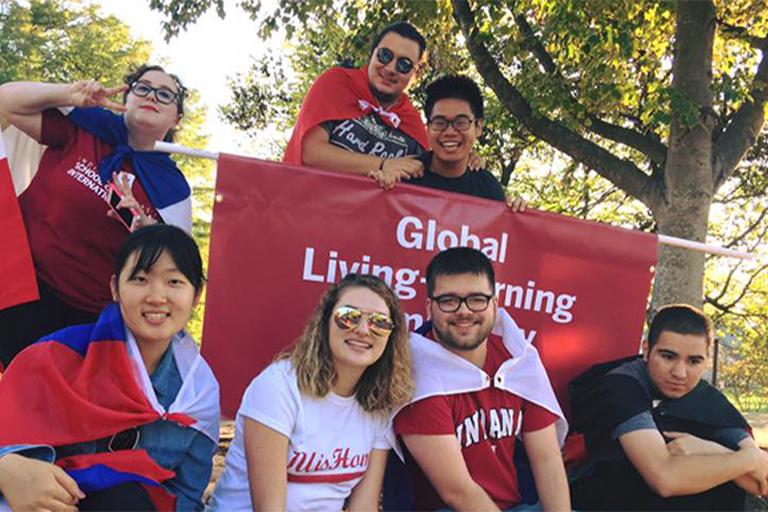 Students wearing flags in front of a sign for the Global Living Learning Center at IU Bloomington.