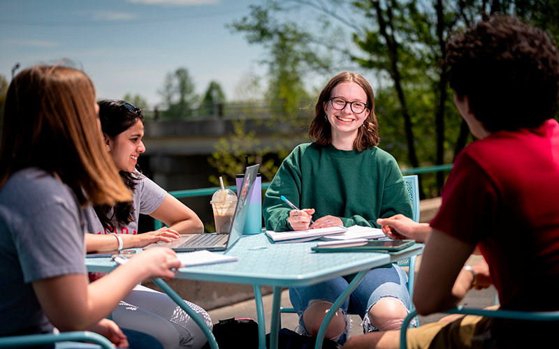 Four students sit at an outdoor table doing homework.