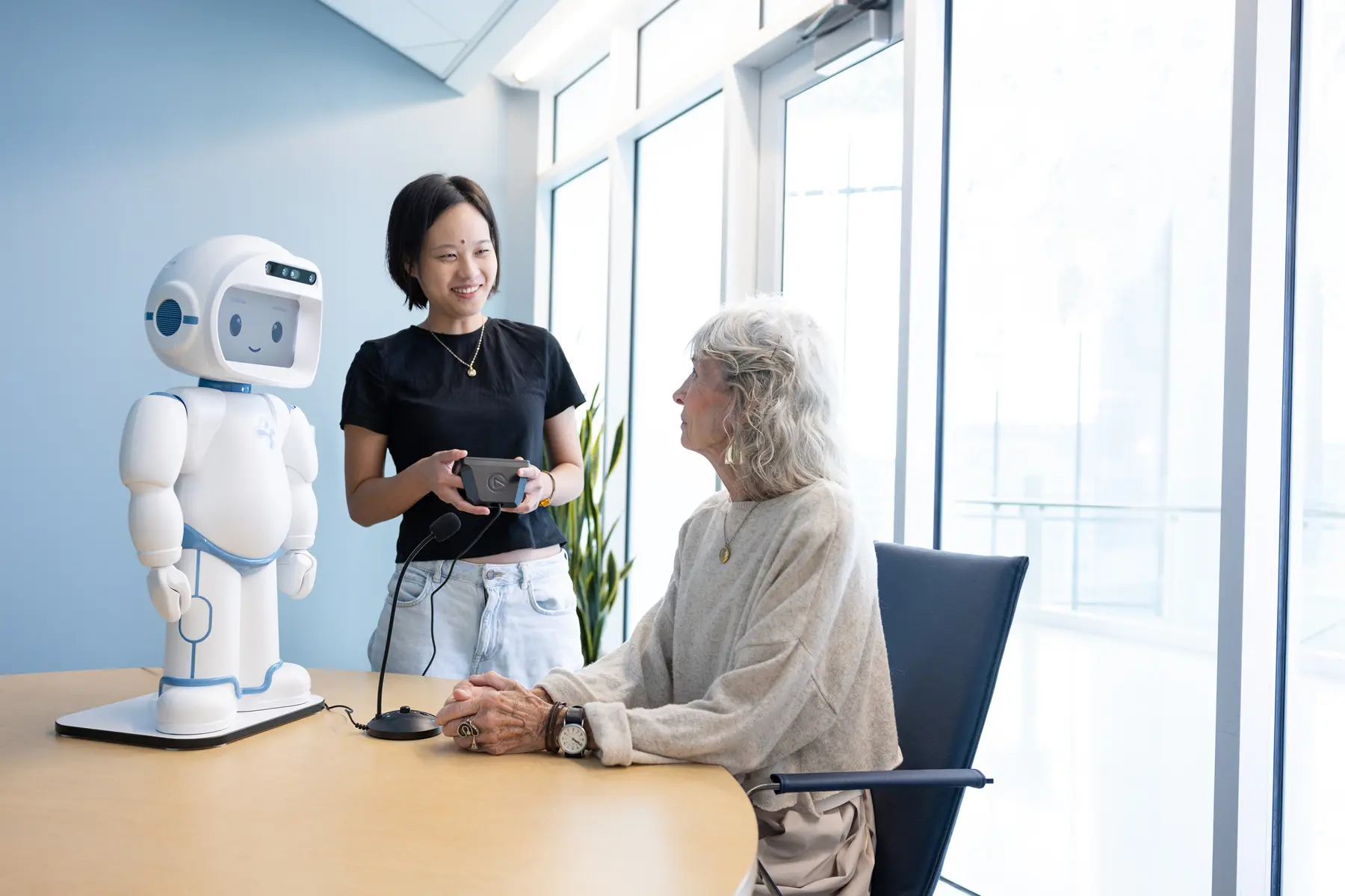 A standing female student demonstrates a robot to a seated female professor.