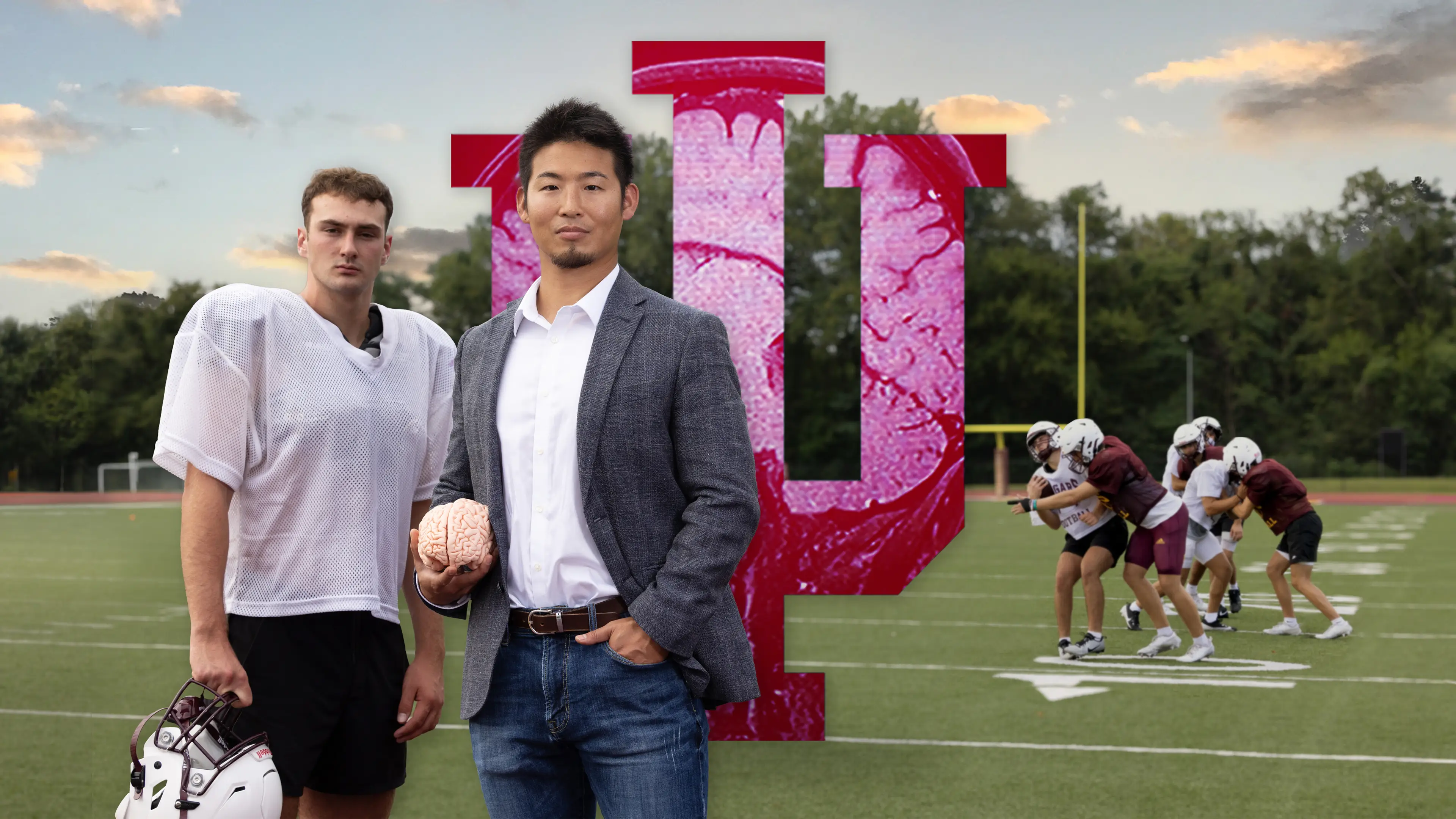 Kei Kawata stands with a high school football player while holding a brain during a scrimmage on a football field