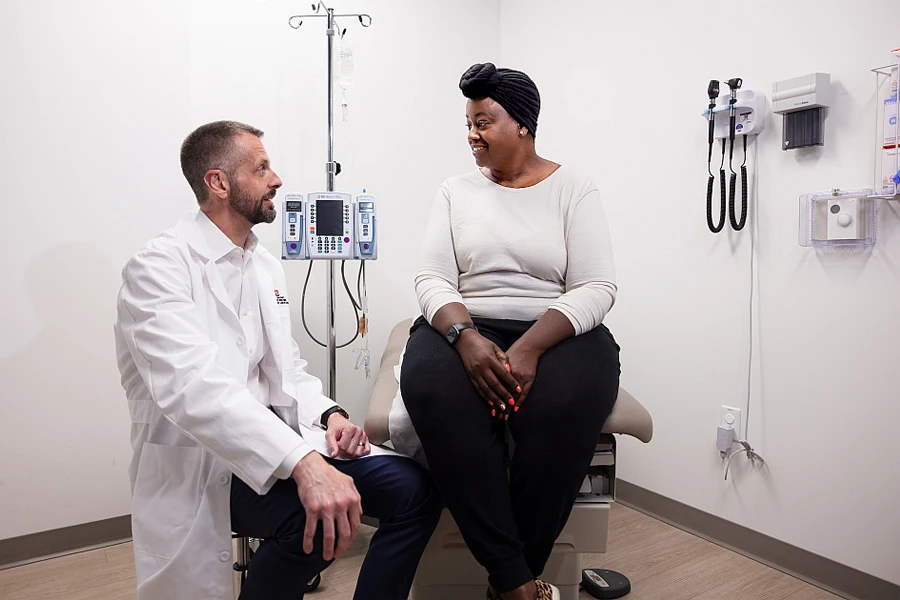 Dr. Bryan P. Schneider consults with a Black breast cancer patient in an exam room.