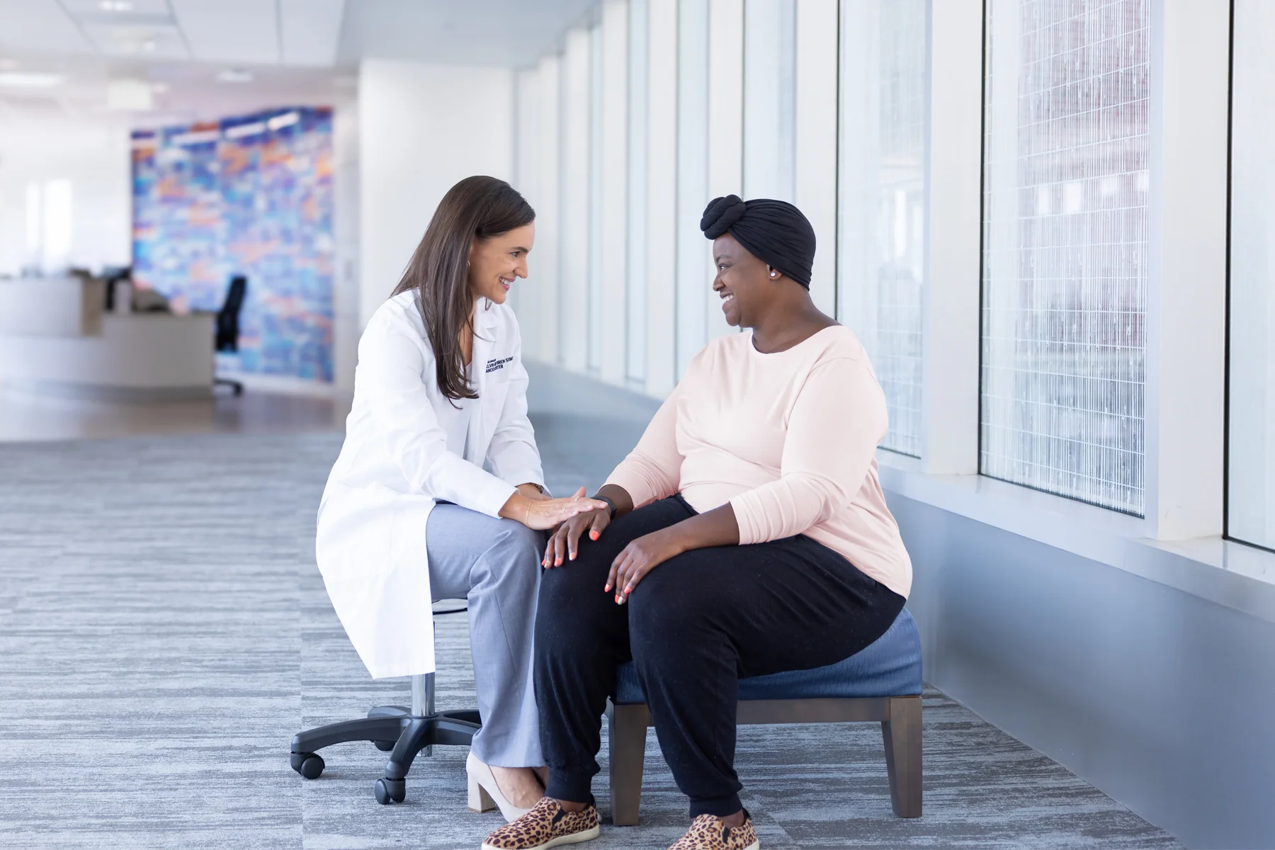 Dr. Tarah Ballinger, MD, sits with a black female breast cancer patient in the bright lobby of the Simon Cancer Center.