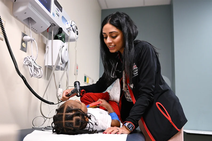 Dr. Seethal Jacob, MD, assistant professor of pediatrics at IU School of Medicine, examines a young black patient on a table.