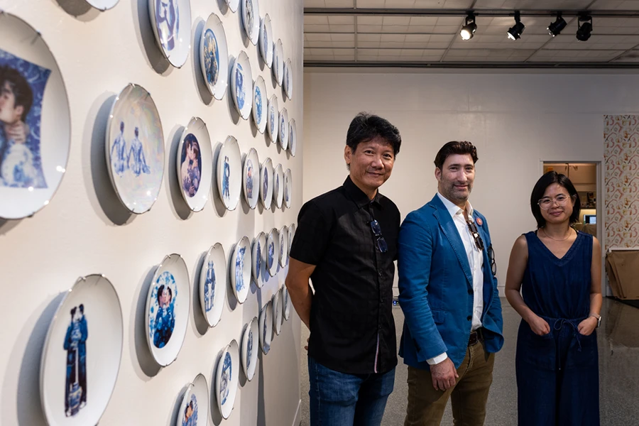 From left, “Blurring the Lines” co-curators Linda Tien and Caleb Weintraub stand with Arthur Liou, director of IU's AI + Digital Futures initiative, in front of artist Adam Chau's piece “Generated Love.” The piece is a cultural commentary on historical representation that employs AI-generated imagery in the style of Ming Dynasty porcelain.