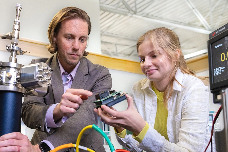 A female student works among electronics equipment with a male faculty member.