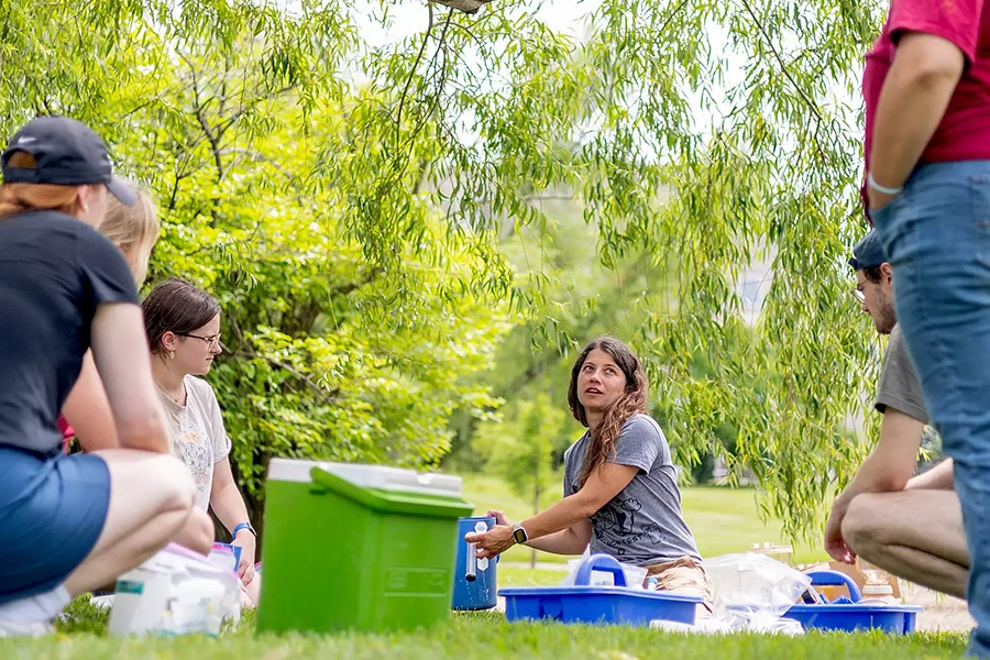 a group of student researchers collect water samples in a grassy area