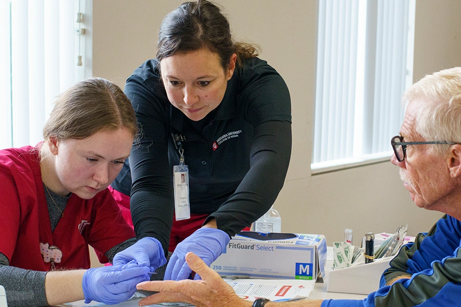 a nursing instructor assists a student in a procedure on a patient