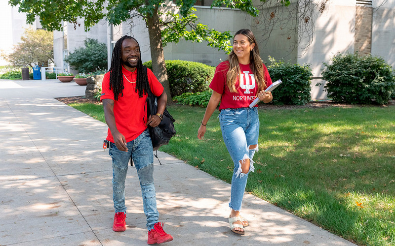 Two students smile as they walk on the IU Northwest campus. One of them wears an IU Northwest shirt.