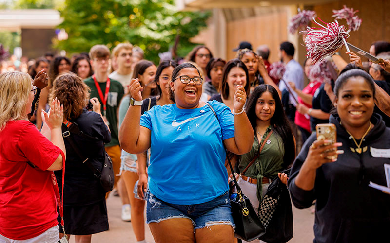 Students smile and walk in a group as faculty and staff cheer for them at an IU South Bend welcome event.