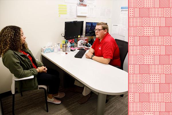 A student is seated in a chair while meeting with an IU staff member in their office.